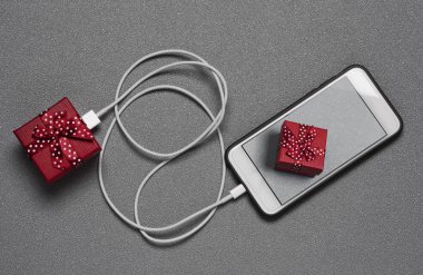 yüksek açılı görünüş aynı hediye onun ekranında, gri bir yüzeyinde, alışveriş online kavramı tasvir eden bir resim ile bir akıllı telefon için bir kablo ile bağlı bir hediye