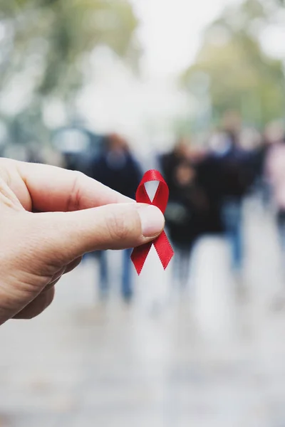 都市のにぎやかな歩行者通りの若い白人男の手にエイズに対する戦いのための赤いアウェアネス リボンのクローズ アップ — ストック写真