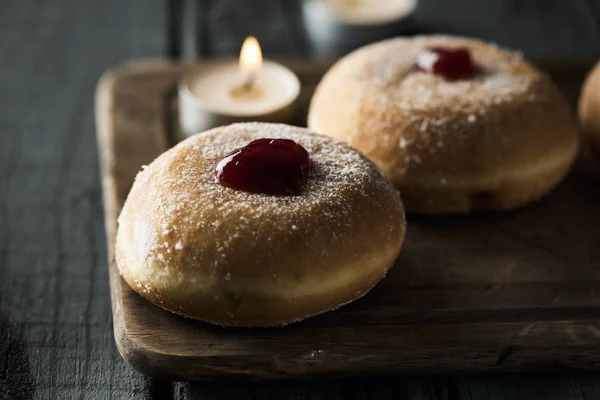 Sufganiyot 的特写 犹太甜甜圈充满了草莓果冻传统上吃的光明节 和一些点燃的蜡烛 在一个质朴的木桌上 — 图库照片