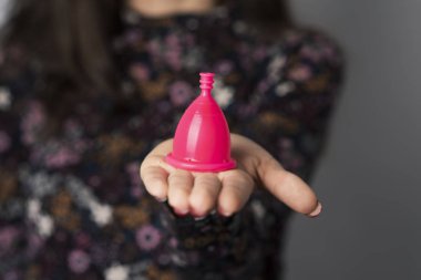 closeup of a young caucasian woman with a pink menstrual cup in her hand clipart
