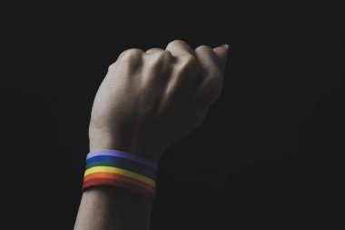 closeup of a young caucasian woman with a rainbow-patterned ribbon tied to his wrist, against a black background clipart
