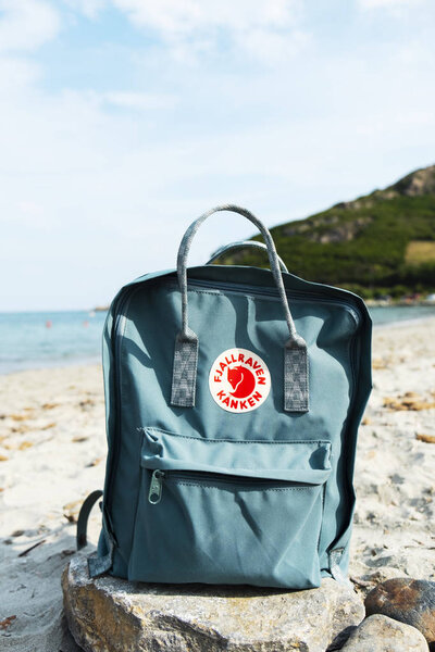 Таррагона, Испания - 16 сентября 2018 года: Популярный рюкзак Фьялравен Канкен на скале, на тихом пляже в Таррагоне, Испания. Это самый продаваемый продукт шведской компании Fjallraven
