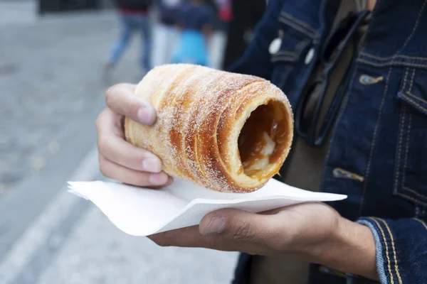 closeup of a yougn caucasian man eating a trdelnik, a typical spit cake, in the old town of Prague, Czech Republic