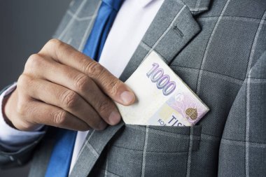 Genç bir beyaz işadamı, zarif bir gri takım elbise giymiş, koyarak veya bazı Çek korunası banknotlar ceketinin cebinde kapalı alarak closeup