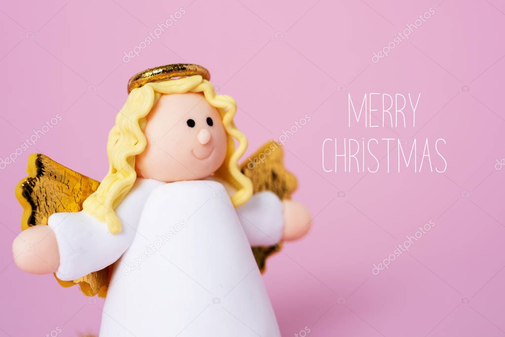 closeup of a handmade angel and the text merry christmas against a pink background