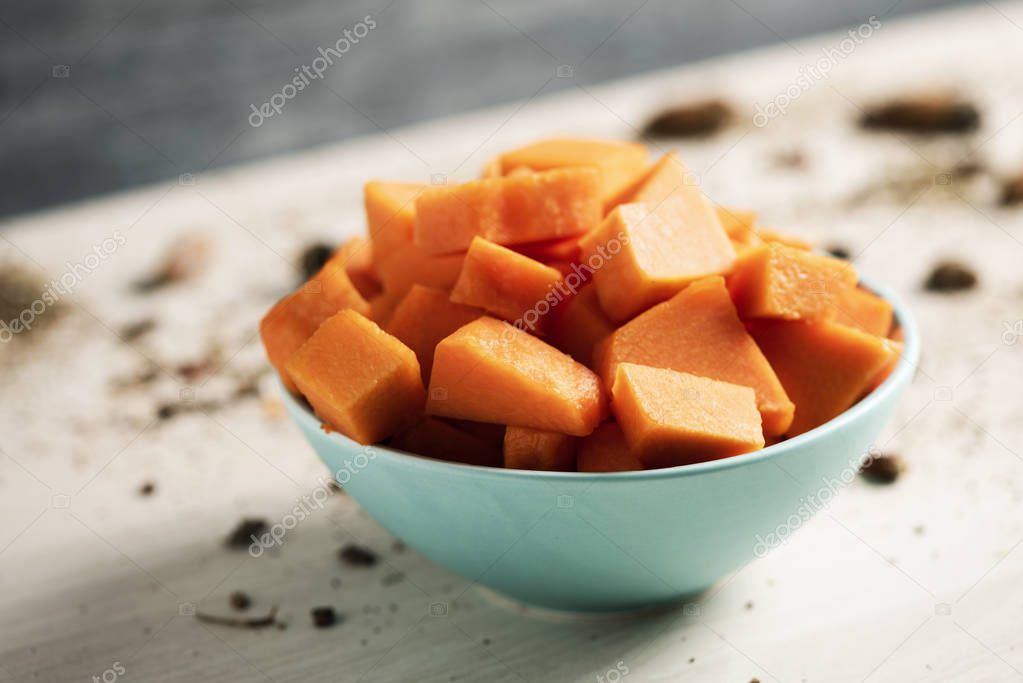 closeup of a pile of chopped raw pumpkin in a pale green bowl placed on a wooden table
