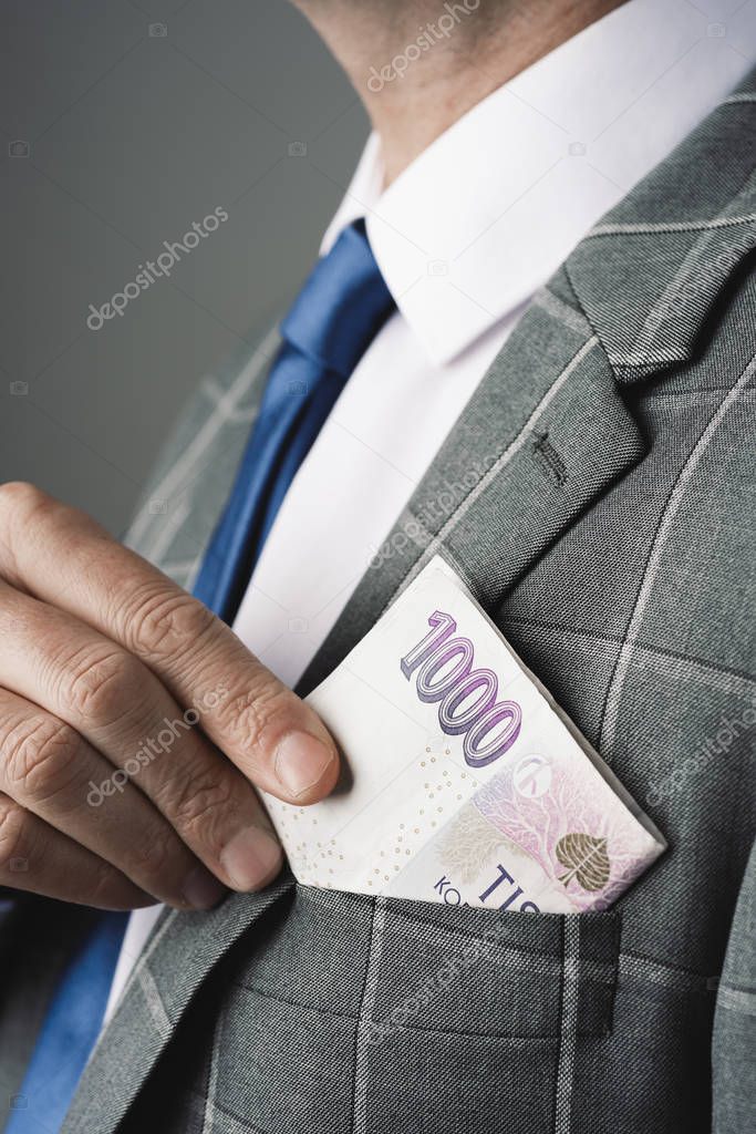 closeup of a young caucasian businessman, wearing an elegant gray suit, putting in or taking off some czech koruna banknotes in the pocket of his jacket