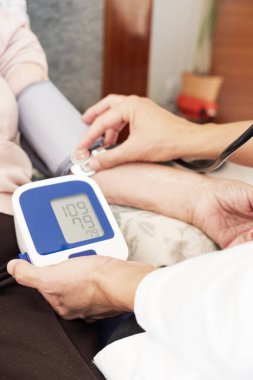 Onu eve veya bir bakım evinde bir tansiyon aleti ile hasta kadın kıdemli beyaz kan basıncı ölçme bir beyaz doktor adam, beyaz bir ceket, closeup