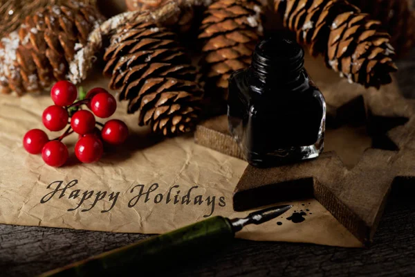 いくつか自然な居心地の良いクリスマスの飾り 松ぼっくりや赤い果実 古い一枚の紙でペン先ペンで書かれたテキストの幸せな休日などのクローズ アップ — ストック写真