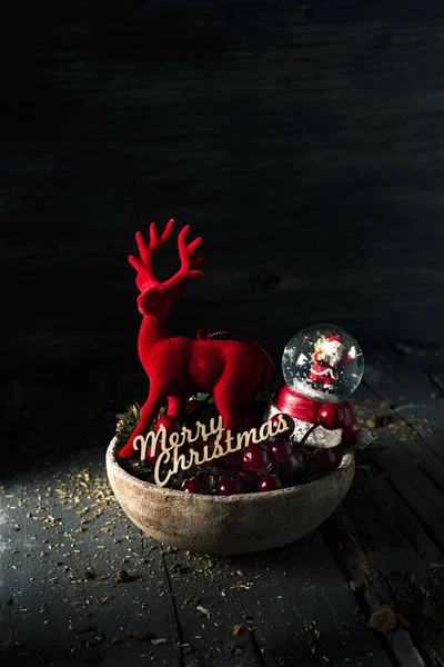 一些不同的圣诞饰品在质朴的棕色陶器托盘和文本快乐的圣诞节在一个质朴的木质表面上的三维 — 图库照片