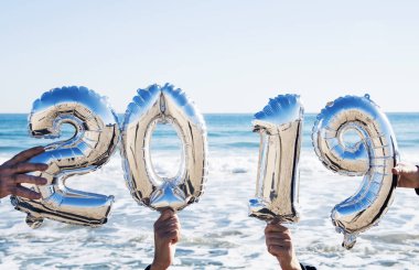 Açık havada numarası 2019, yeni yıl ve okyanusun içinde belgili tanımlık geçmiş olarak oluşturan gümüş bazı sayı şeklindeki balonları tutan elleriyle