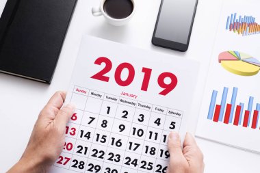 2019, bazı grafikler, bir fincan kahve, bir smartphone ve a not etmek yanında takvimini gözlemleyerek onun ofis masasında oturan bir beyaz adam görünümünü yüksek açı