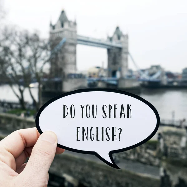 一个年轻的高加索人拿着一个对话泡沫形状的招牌的特写镜头 有一个问题 你会说英语吗 写在它 在伦敦的塔桥前 — 图库照片