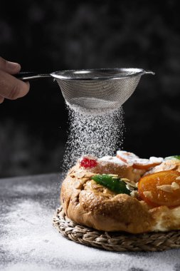 beyaz bir adam bir roscon de biraz pudra şekeri yağmurlama closeup reyes, gri bir rustik masada yer Epifani günde yenen bir İspanyol üç Kral kek