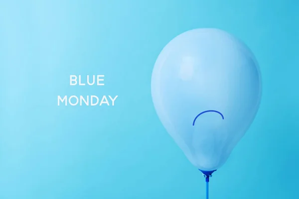 closeup of a blue balloon, with a sad face drawn in it, and the text blue monday on a blue background