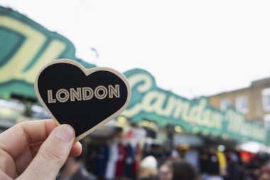 closeup of a caucasian man holding a black heart with the word london written in it, in front of the popular the camden market, in camden high street, in london, united kingdom clipart