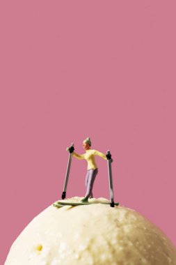 a miniature skier on an ice cream ball, against a pink background with some blank space on top