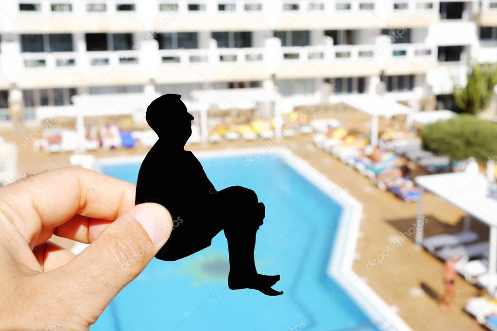 closeup of the hand of a man with a black paper cutout in the shape of a man throwing himself into a swimming pool