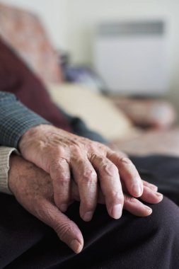 Kafkasyalı yaşlı bir adamla beyaz bir kadının kanepede oturup sevgiyle el ele tutuşmaları.