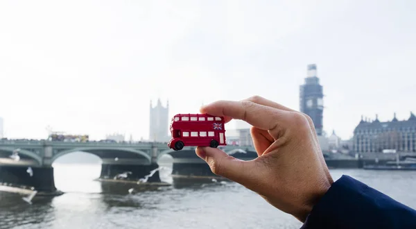 一个白种人拿着一辆红色双层巴士的缩影 典型的是英国伦敦 背景是威斯敏斯特大桥和威斯敏斯特宫 — 图库照片