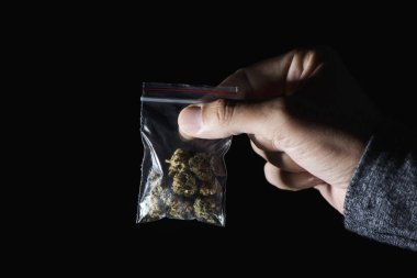Biraz esrar tomurcukları elinde siyah bir arka plan biraz boş alan ile bir plastik torba ile genç bir beyaz adam closeup