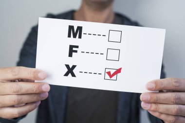 bir form içinde bir onay işareti x ile yazılmış üçüncü cinsiyet kategorisinin için erkek, kadın ve X F M harfleri ile tutan genç bir beyaz kişi closeup