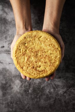 bir tipik tortilla de patatas, İspanyol omleti, beyaz bir adamla yüksek açılı görünüş gri taş yüzeyi ellerinin üstünde