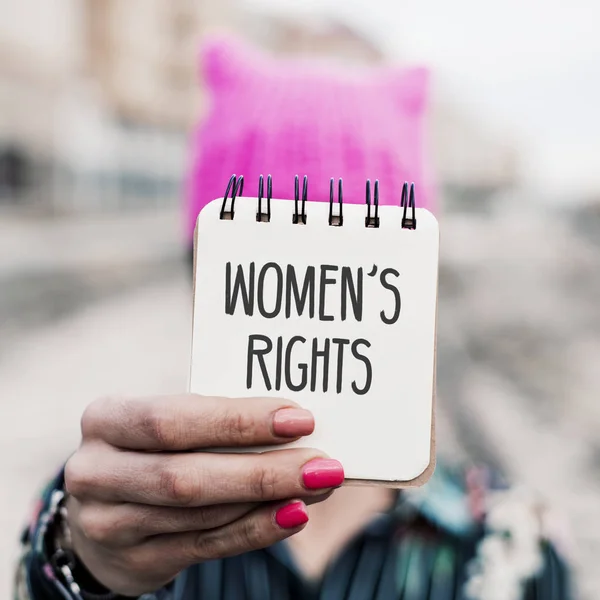 屋外で書かれたテキストの女性の権利の彼女の顔の前で紙を示すピンク プッシーキャット帽子を着た若い女性のクローズ アップ — ストック写真