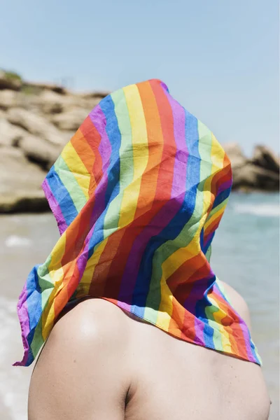 Uomo con una bandiera arcobaleno di fronte all'oceano — Foto Stock