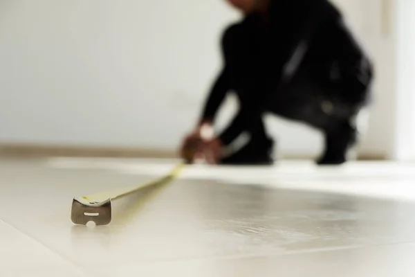 Homem usando uma fita métrica em um piso de azulejos — Fotografia de Stock