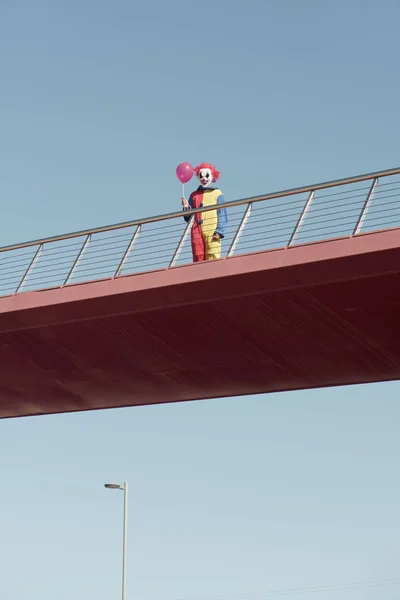 Enge clown met een rode ballon op een brug — Stockfoto