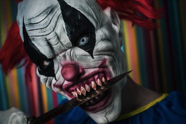 scary evil clown with a knife in his mouth