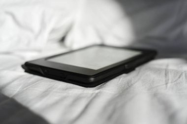 Yapılmamış bir yatakta tablet ya da e-okuyucu