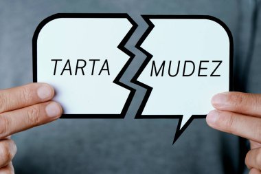 Kırık bir konuşma balonu gösteren genç beyaz bir adamın yakın çekimi, İspanyolca yazılmış bir metin kekelemesi.