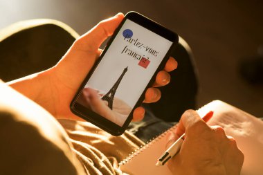Kafkasyalı bir gencin resmi, günlük kıyafetler giymiş, koltuğa oturmuş, akıllı telefonu elinde metinle ekranında Fransızca konuşuyor musunuz?