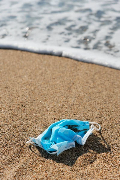 Zbliżenie Niebieskiej Używanej Maski Chirurgicznej Rzuconej Mokry Piasek Wybrzeżu Plaży — Zdjęcie stockowe