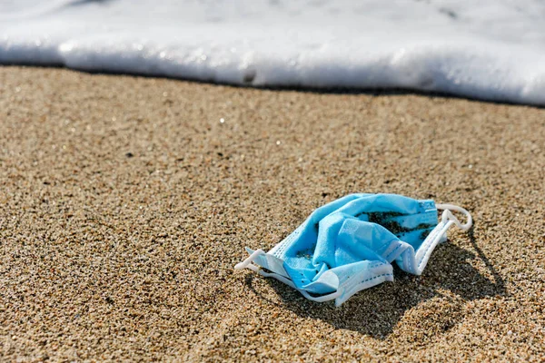 Plajın ıslak kumlarına atılmış mavi ameliyat maskesine yakın plan.