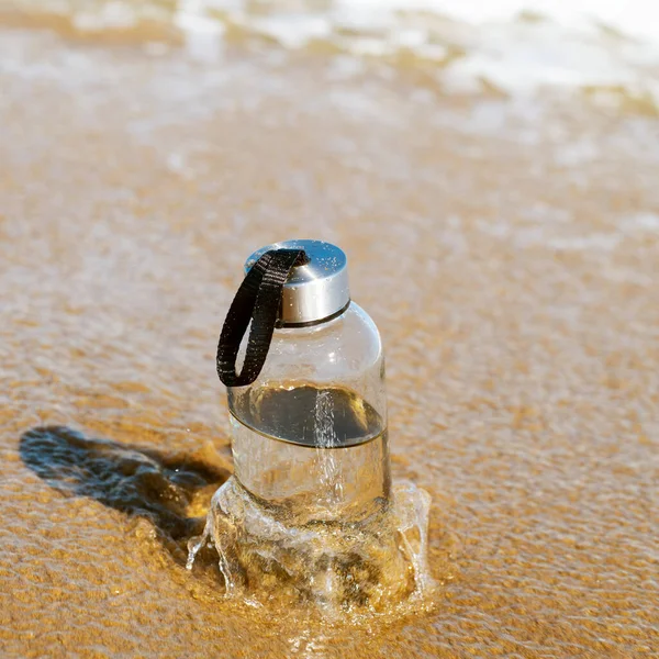 孤独なビーチの海岸にあるガラスの再利用可能な水ボトルの閉鎖 — ストック写真