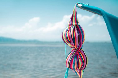 closeup of the top of a colorful bikini drying on a blue deck chair next to the water of the ocean or a lake clipart