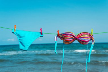 Sahilde çamaşır ipinde asılı duran iki parça bikini. Arka planda deniz var.