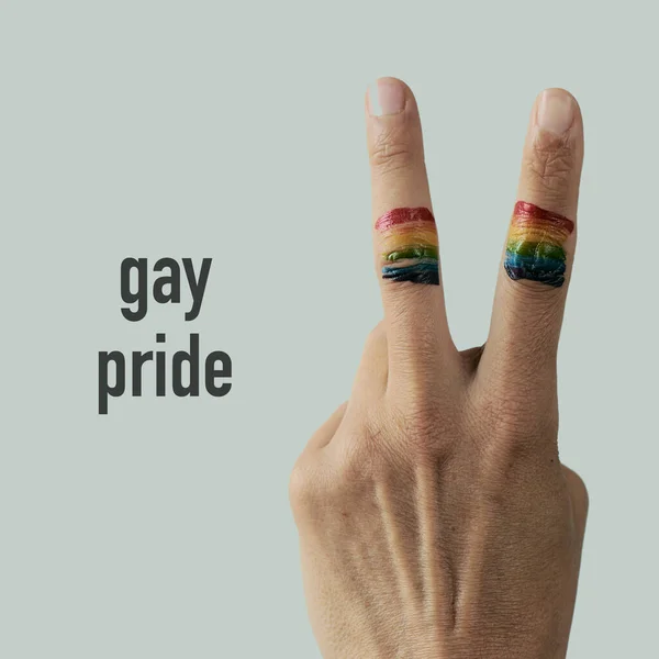 Vサインをした若い白人男性の指に虹の旗が掲げられゲイのプライドが白色の背景に向けられました — ストック写真