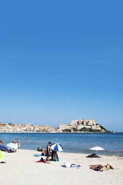 CALVI, FRANCE - 21 SEPTEMBER 2018: İnsanlar Calvi, Corsica, Fransa 'da plajın tadını çıkarıyorlar, ünlü kalesi arka tarafta bir promontuarın tepesinde.