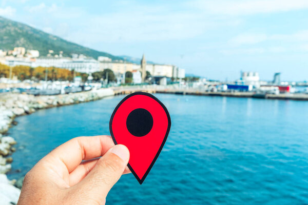 the hand of a young caucasian man with a red marker pointing the port of Bastia, in Corsica, France, with the commercial port on the right and the Notre-Dame de Lourdes church in the background