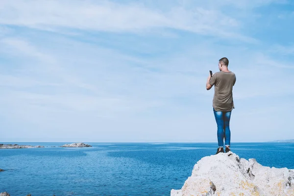 フランスのコルシカ島南岸の海をスマートフォンで撮影した岩の上から見た若い白人男性が — ストック写真