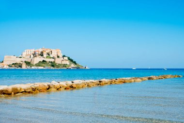 Fransa, Korsika 'da Calvi' nin ünlü kalesi bir promontuarın tepesinde ve ön planda Akdeniz manzarası.