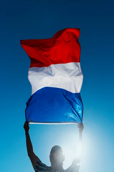 青い空に向かって風になびくフランス国旗を背負った青年のシルエットのクローズアップ — ストック写真