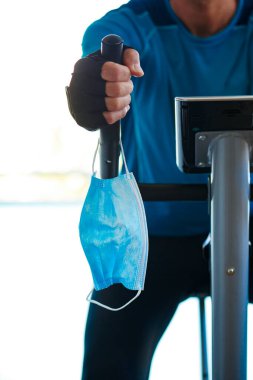 Spor giyim kuşamında, durağan bisiklet kullanan ve giyerken gidonu giyerken maskesini giyemeyen beyaz bir gencin yakın çekimi.