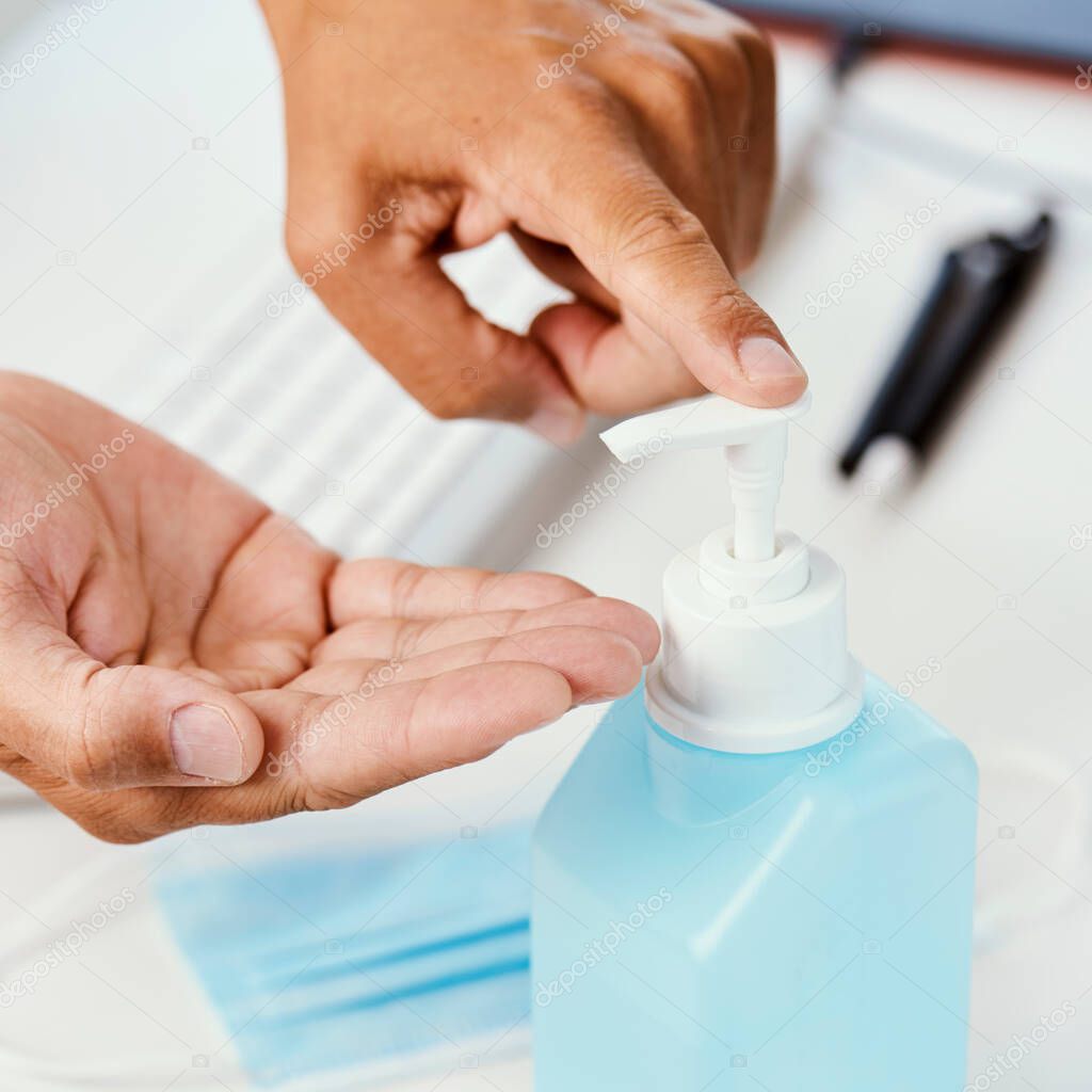 closeup of a young caucasian man at his office desk disinfecting his hands with hand sanitizer from a blue bottle