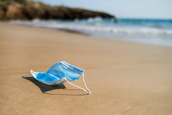 青い使用済みの外科用マスクを閉じて海に連れ戻された孤独なビーチの海岸の湿った砂の上に — ストック写真