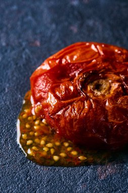 Soyulmamış kavrulmuş bir domatesin yakın çekimi ve suyu ve tohumları siyah bir taş yüzeyine döküldü.